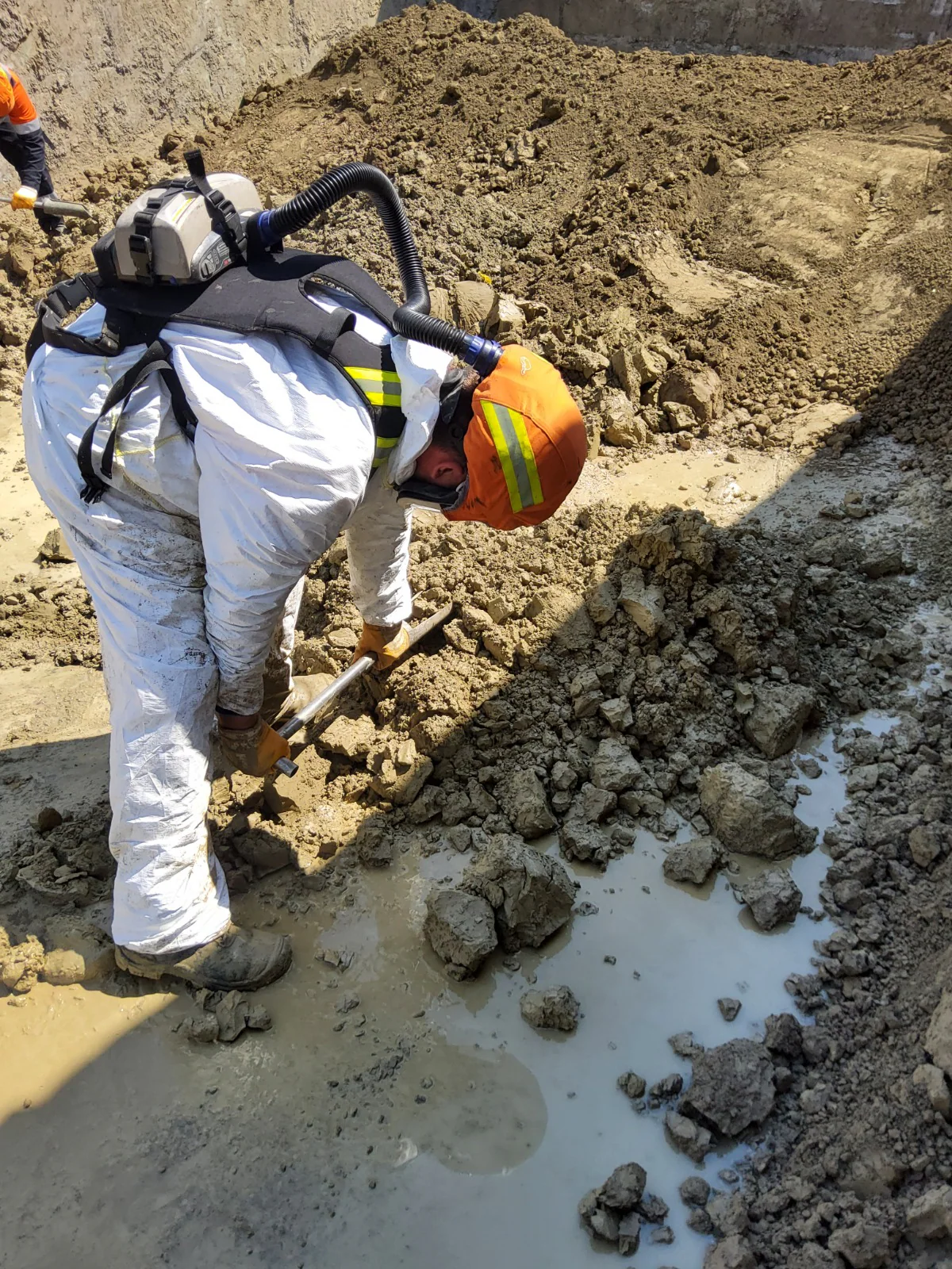 Surveyor manually sampling wet material while wearing protective equipment